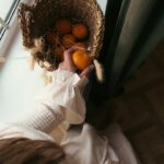 a person holding a basket of oranges in front of a window