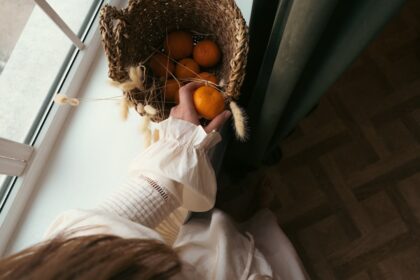 a person holding a basket of oranges in front of a window