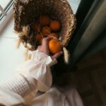 a person holding a basket of oranges in front of a window
